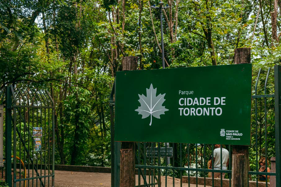 Imagem da entrada do Parque Cidade de Toronto. A entrada tem uma placa verde com o nome do parque e suas grades também são verdes