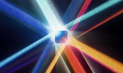 A imagem mostra uma composição abstrata com um foco luminoso central, onde um quadrado translúcido parece refratar a luz. A partir desse centro, feixes de luz coloridos se espalham em várias direções, formando raios em tons de azul, ciano, vermelho, laranja e amarelo.