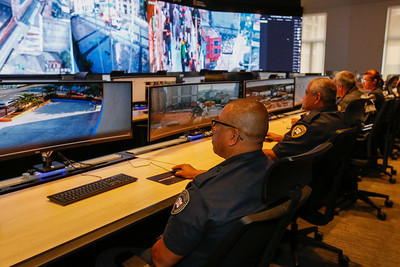 Foto mostra uma tela grande com várias imagens de ruas. Mostra tamém mesas commonitores e guardas municipais sentados a frente fazendo o monitoramento das imagens.