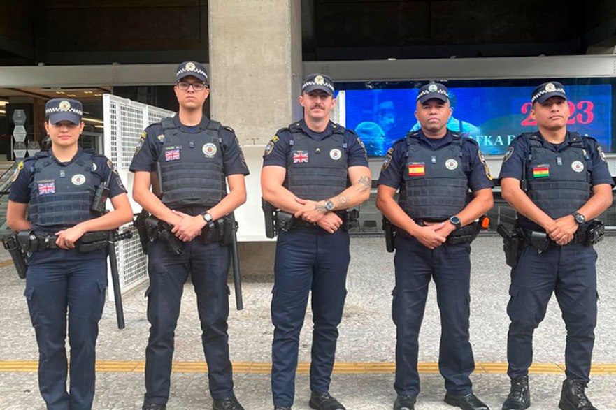 Cinco Guardas Civis Metropolitandos biligues com bandeira no peito representando o pais para que os turistas identifiquem
