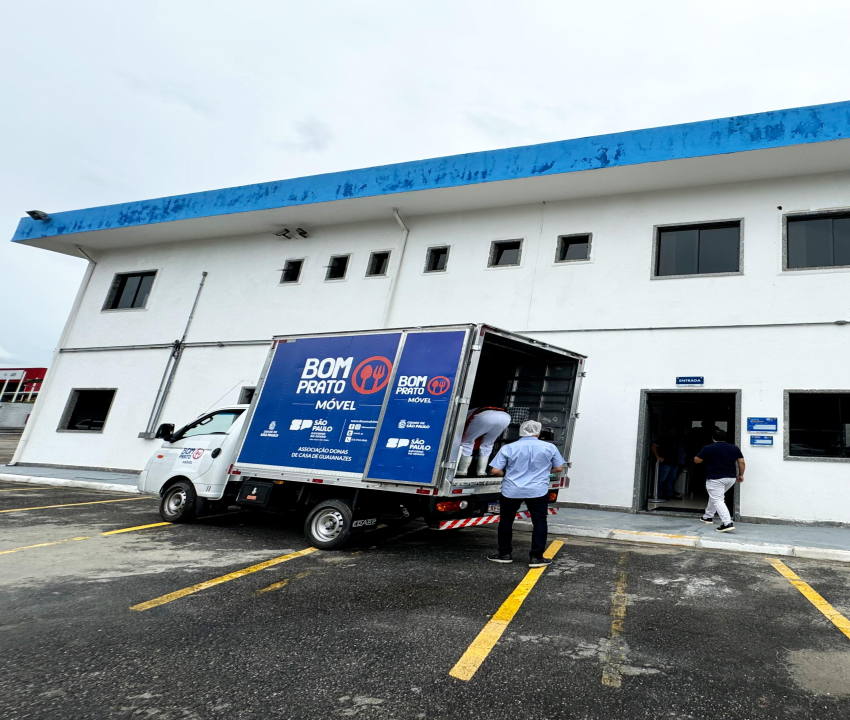 funcionários fazendo entrega de marmitex com o caminhão BOM PRATO Móvel estacionado em frente ao prédio bom prato da cidade tiradentes