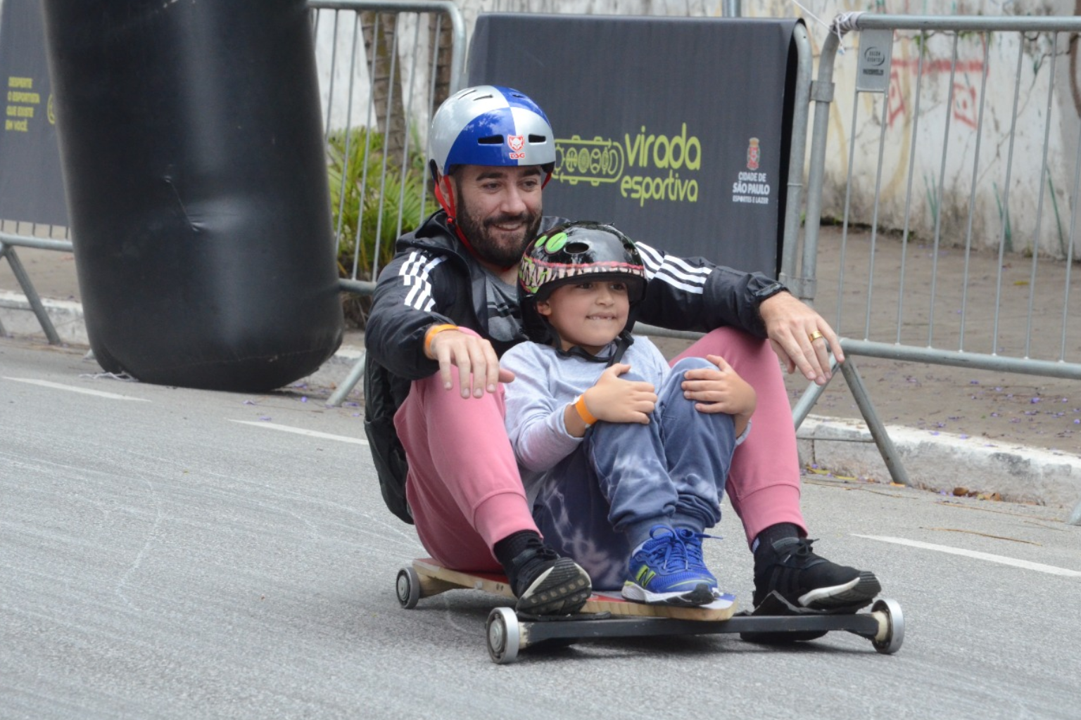 Imagem de um adulto junto a uma criança descendo uma ladeira de carrinho de rolimã
