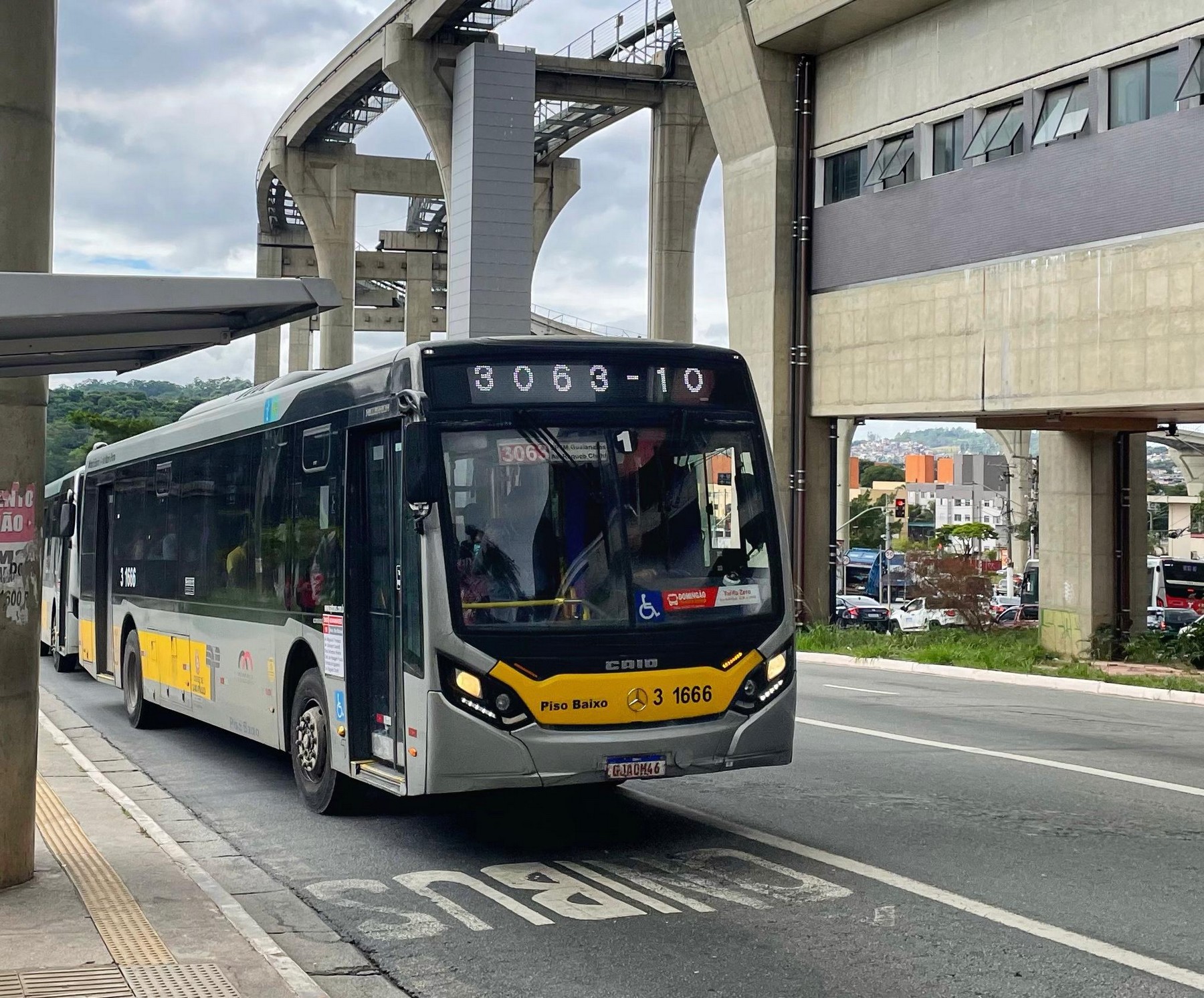 #PraTodosVerem: Imagem do ônibus da linha 3063-10 Guaianases - Term. São Mateus, na cor amarela, em frente a um ponto de ônibus na avenida Ragueb Chohfi. Ao fundo, é possível ver o monotrilho.