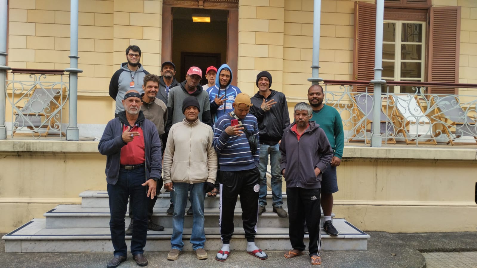 Imagem de um grupo de homens posando para uma fotos, eles estão reunidos em uma escadaria em frente a uma entra de museu 