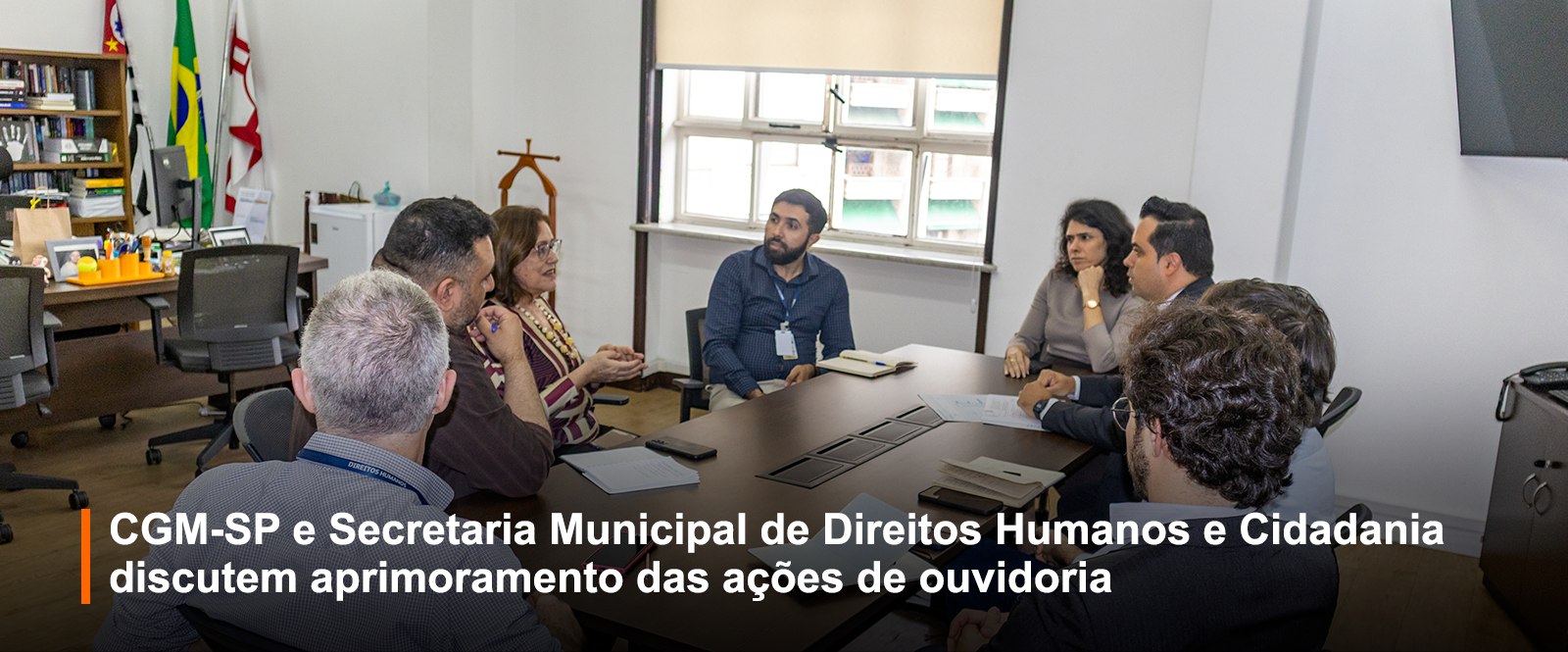 Foto de uma reunião com 8 pessoas dentro de uma sala