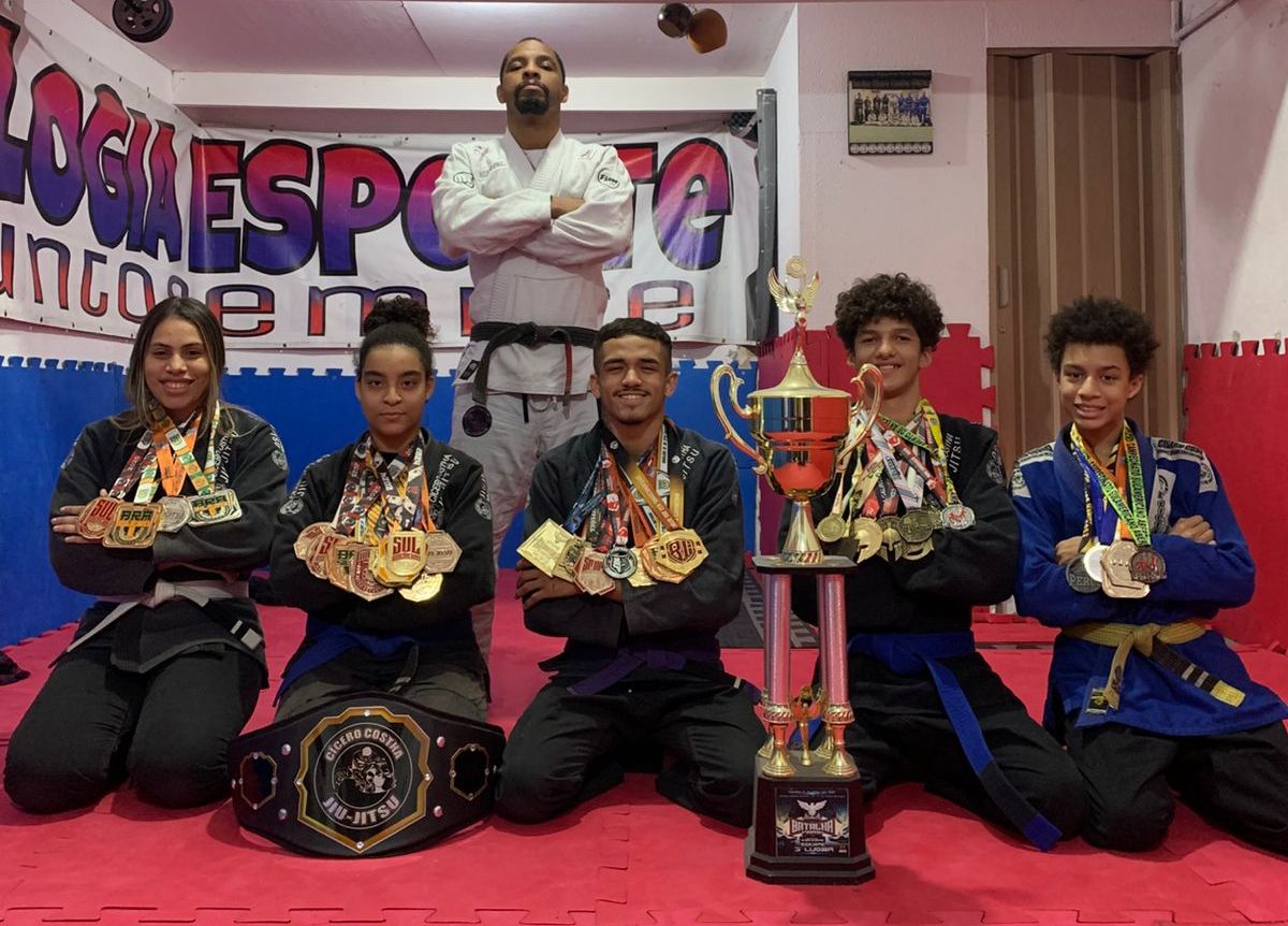 Na imagem, atletas de jiu-jitsu posando com suas medalhas, junto com o professor.