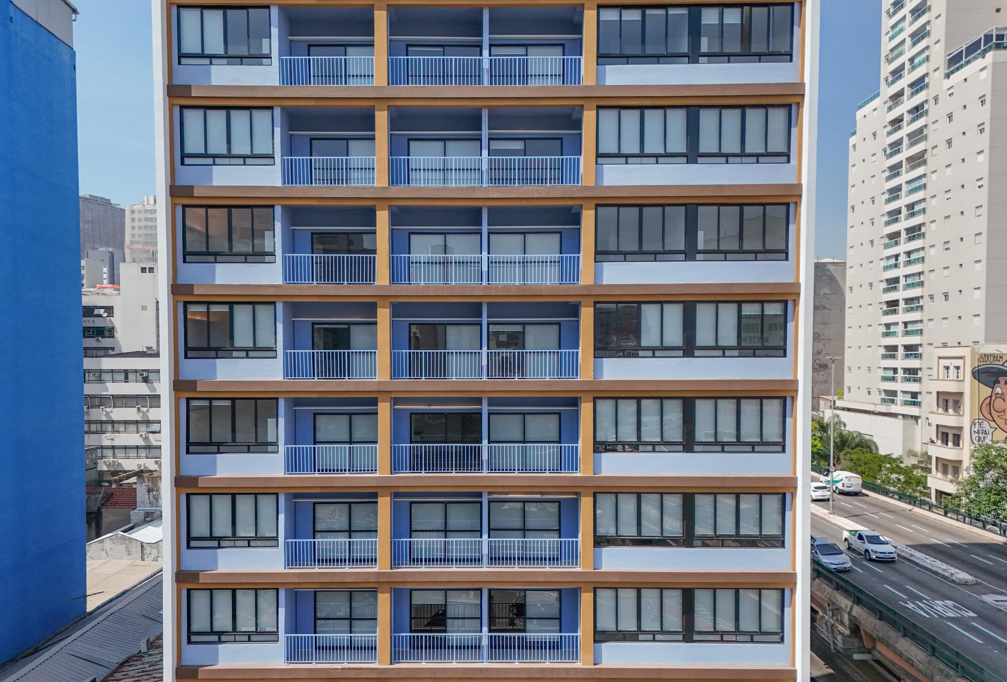Fachada de um prédio residencial reformado, com varandas e janelas alinhadas em tons de azul e bege, localizado em área urbana de São Paulo.