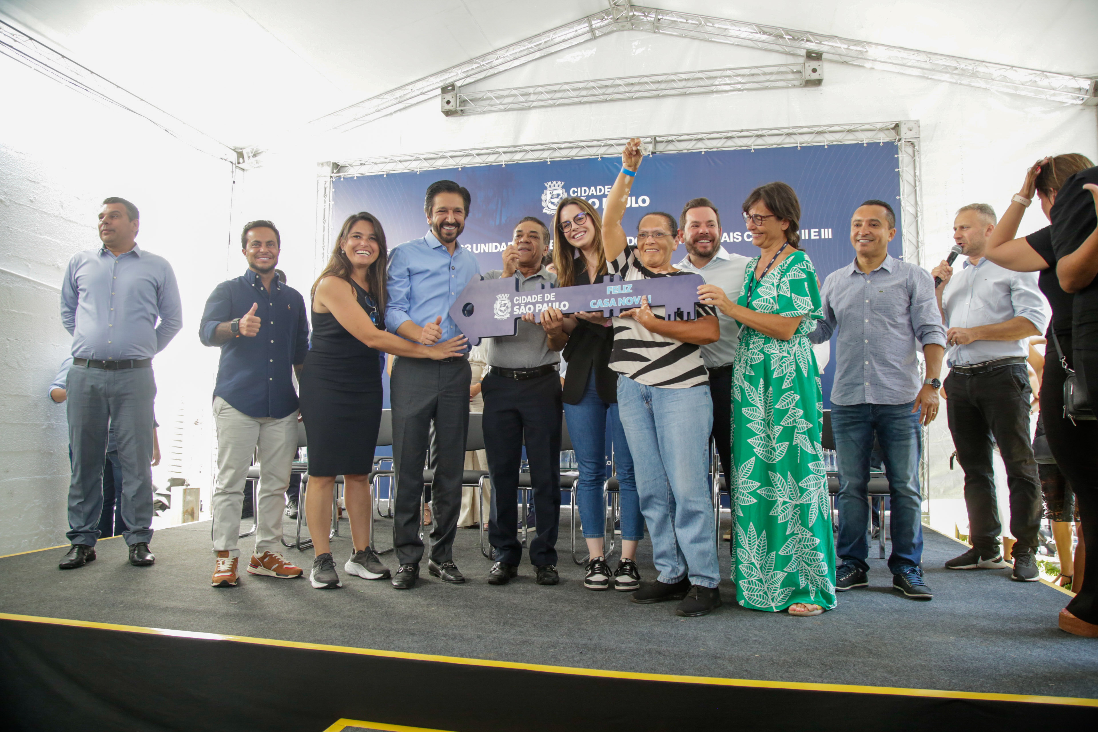 Senhorarecebendo a chave de sua nova moradia junto com o Prefeito Ricardo Nunes e secretários