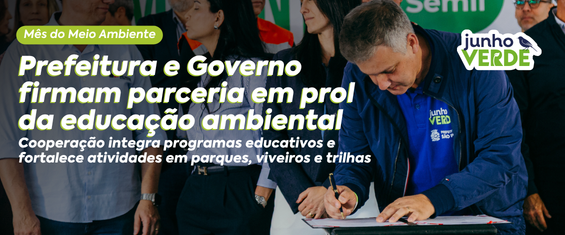Homem assina um documento durante evento oficial, cercado por outras pessoas. Na imagem, destaca-se o anúncio de uma parceria entre Prefeitura e Governo para fortalecer a educação ambiental por meio de programas educativos, parques, viveiros e trilhas, dentro da campanha Junho Verde.