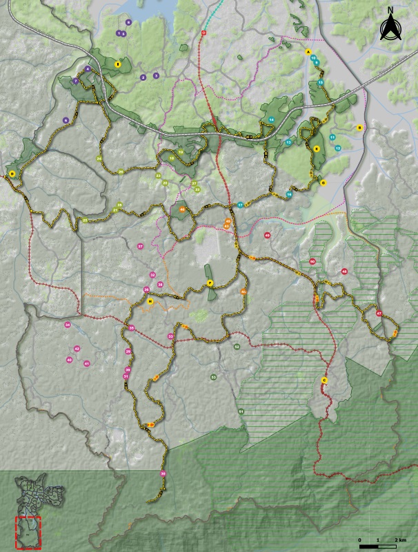 O mapa representa uma grande área natural composta por vários parques interligados por trilhas e caminhos pedestres. Está orientado com o norte para cima (indicado por uma rosa-dos-ventos no canto superior direito). O fundo é em tons de cinzento e verde, sugerindo relevo e zonas de vegetação. No canto inferior esquerdo, há uma miniatura do mapa completo com um quadrado vermelho, mostrando a área destacada no mapa principal.As trilhas estão marcados com linhas coloridas: •	Linhas laranja: caminhos principais, com marcações mais espessas e que percorrem quase toda a área. •	Linhas vermelhas tracejadas: possíveis trilhos secundários ou alternativos. •	Linhas cor-de-rosa, azuis, verdes e roxas: diferentes trilhos temáticos ou rotas específicas dentro dos parques. Os caminhos conectam diversos pontos e parecem cruzar áreas de floresta, montanhas e campos cultivados indicados por zonas com linhas verdes diagonais.
