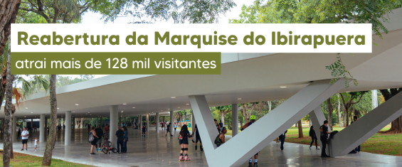 Imagem fotográfica da Marquise do Parque Ibirapuera, em São Paulo, após a reabertura. A estrutura moderna aparece em destaque, com grandes pilares brancos em formato inclinado sustentando a cobertura plana. O piso é amplo e liso, permitindo a circulação de pedestres. Diversas pessoas caminham, conversam ou permanecem no local, algumas sozinhas e outras em pequenos grupos, indicando uso intenso do espaço. Ao redor da marquise, há muitas árvores e áreas verdes, com tons predominantes de verde das copas e do gramado, contrastando com o branco da arquitetura e o cinza do piso. Na parte superior da imagem, há uma faixa com fundo verde-oliva e branco, contendo o texto: “Reabertura da Marquise do Ibirapuera atrai mais de 128 mil visitantes”. O ambiente transmite sensação de convivência, lazer e integração com a natureza.