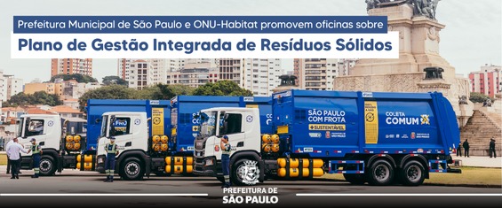 Cinco caminhões de coleta de resíduos sólidos, da frota da Prefeitura de São Paulo, estão alinhados lado a lado no Parque da Independência, em frente ao Monumento à Independência. Os veículos são azuis, com os dizeres 