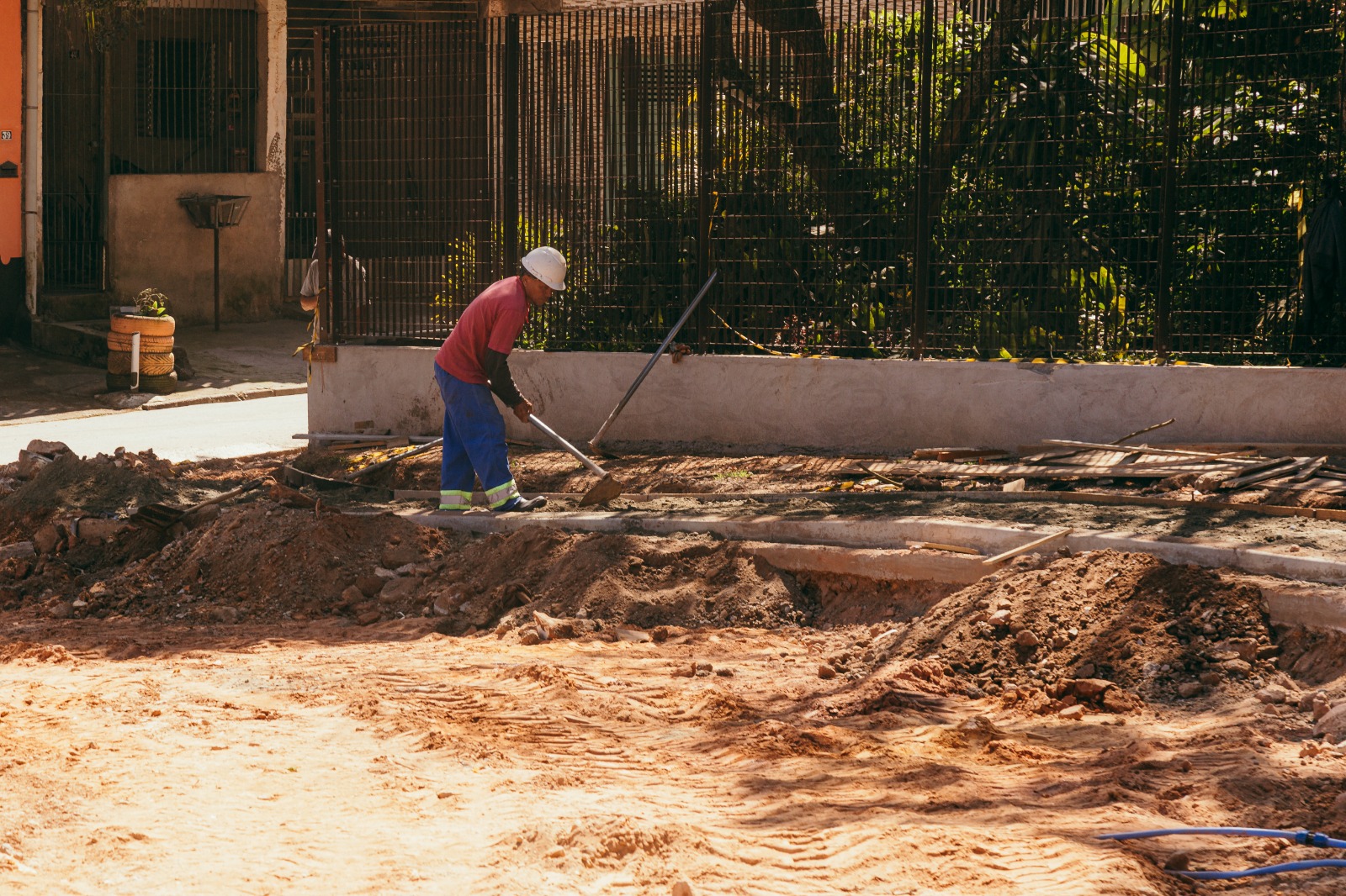 Trabalhador da construção civil, usando capacete e equipamentos de proteção, realiza atividades em uma obra ao ar livre, contribuindo para a melhoria da infraestrutura urbana.