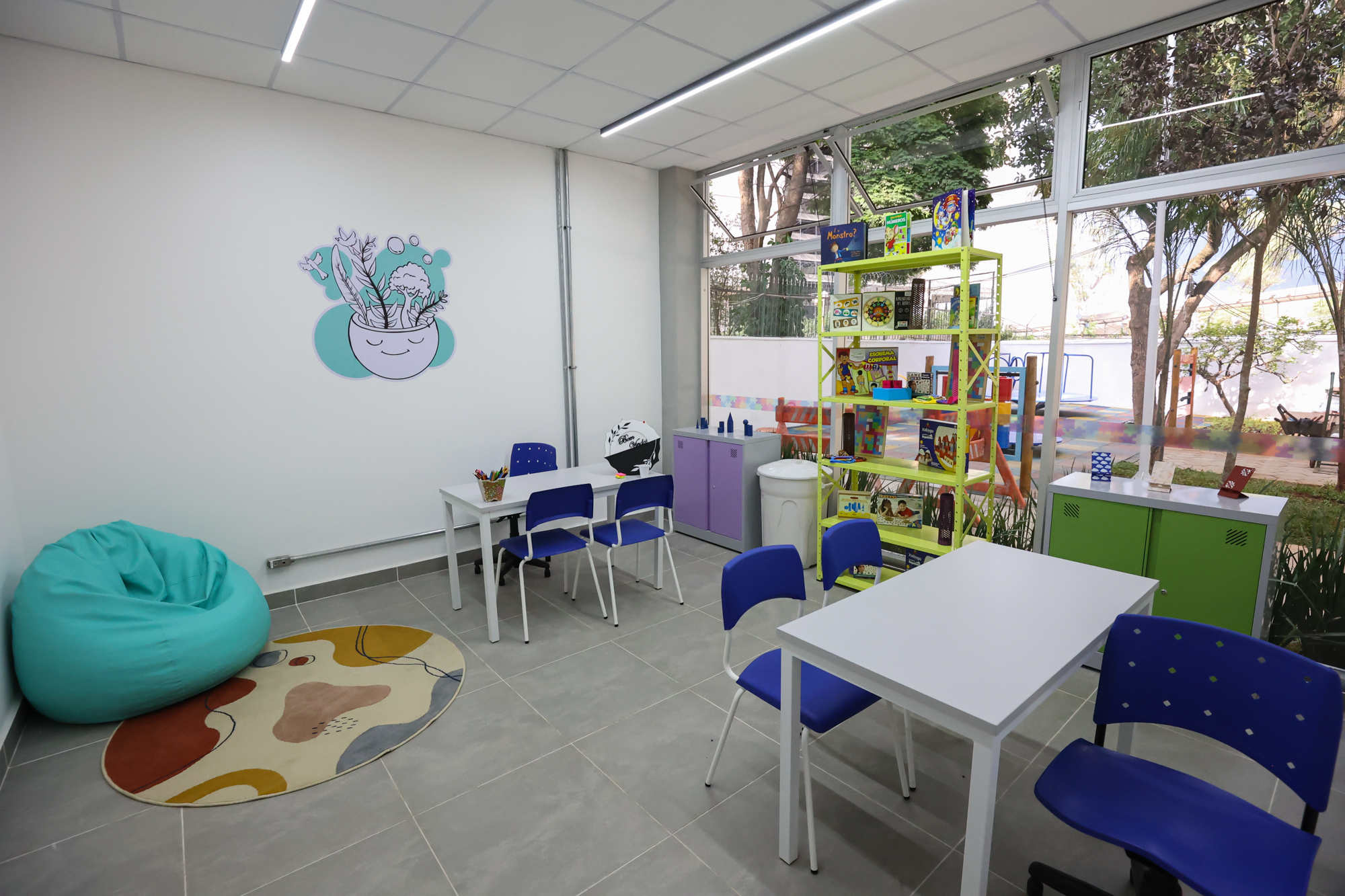 Imagem da sala de atendimento e orientação do Centro TEA. Nela há uma estante com livros, mesas, cadeiras e armários.