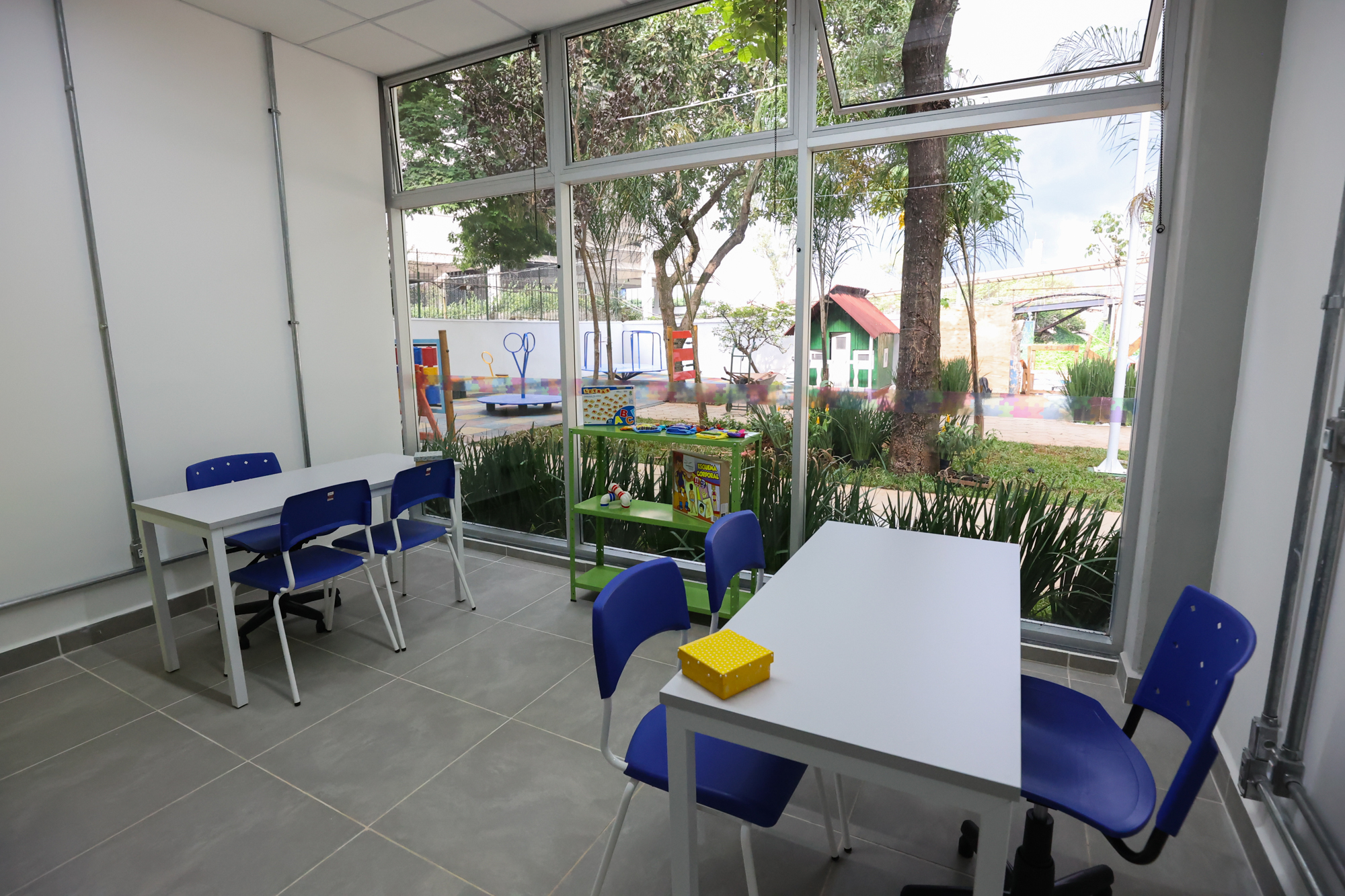 Imagem da sala de atendimento e orientação do Centro TEA. Nela há uma estante com livros, mesas, cadeiras.
