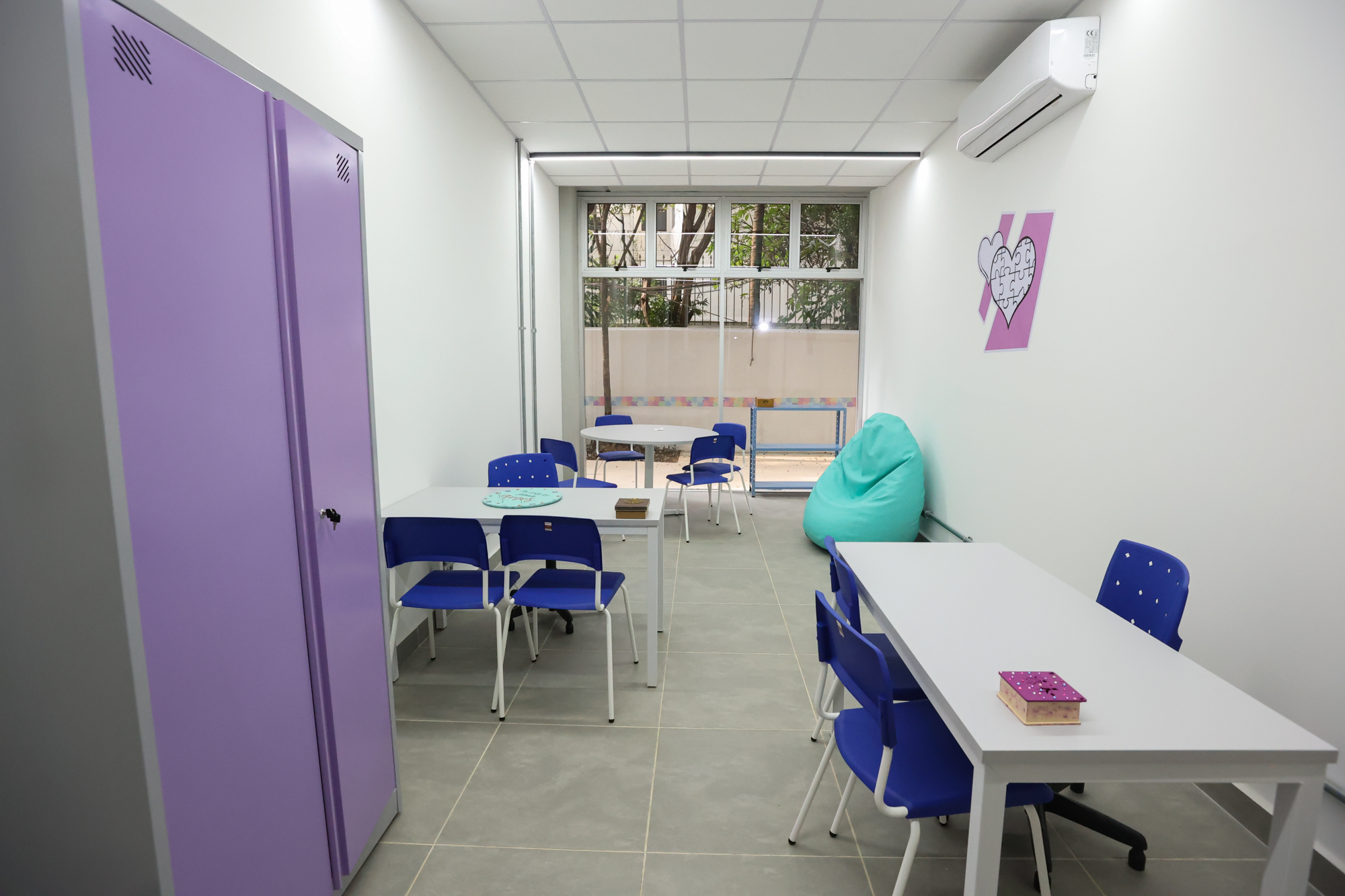 Imagem da sala de atendimento e orientação do Centro TEA. Nela há mesas, cadeiras, armário e puff.