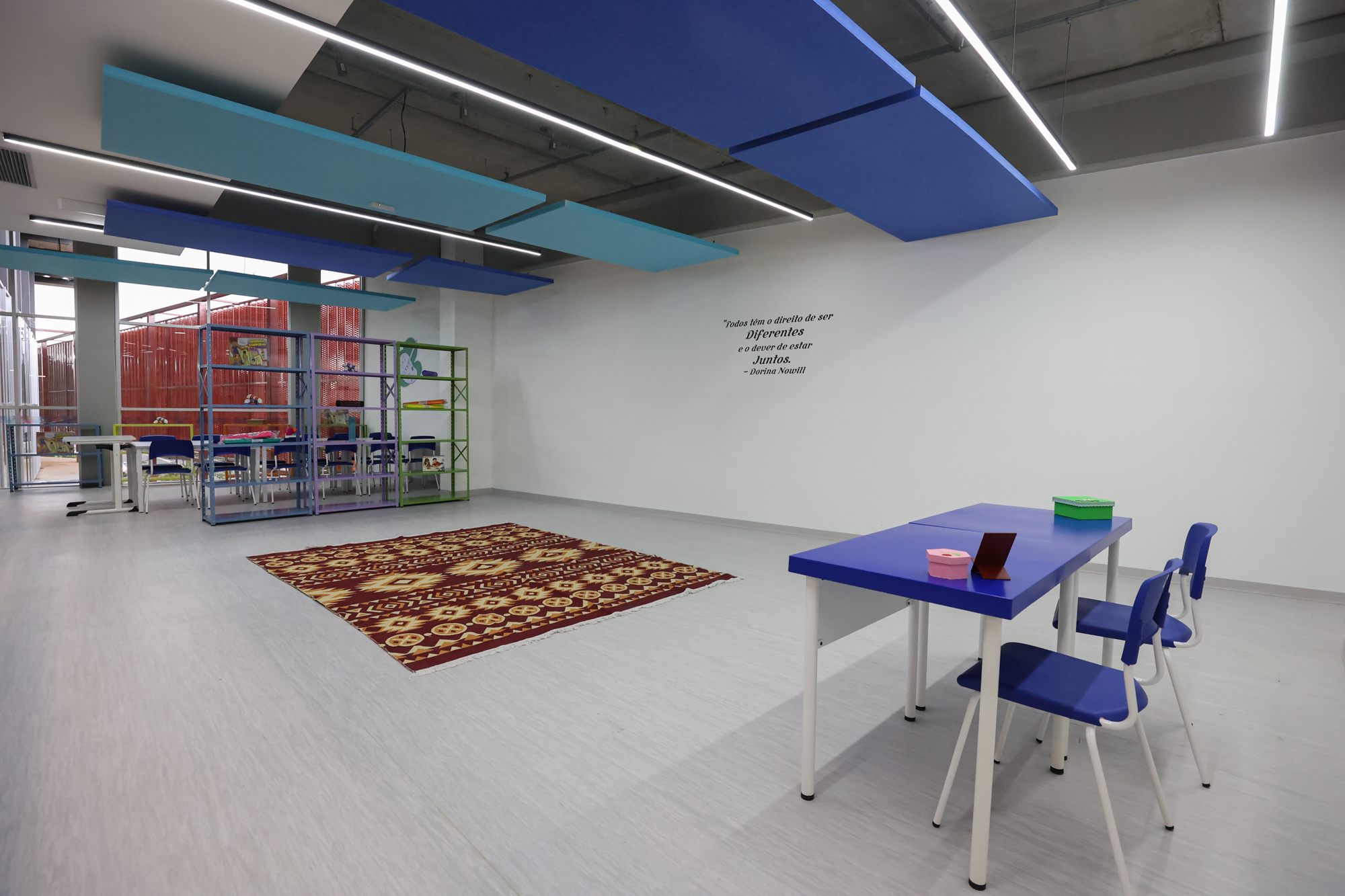 Imagem da sala de oficinas do Centro TEA. Nela há mesas, cadeiras, armários, estante com objetos e tapete.