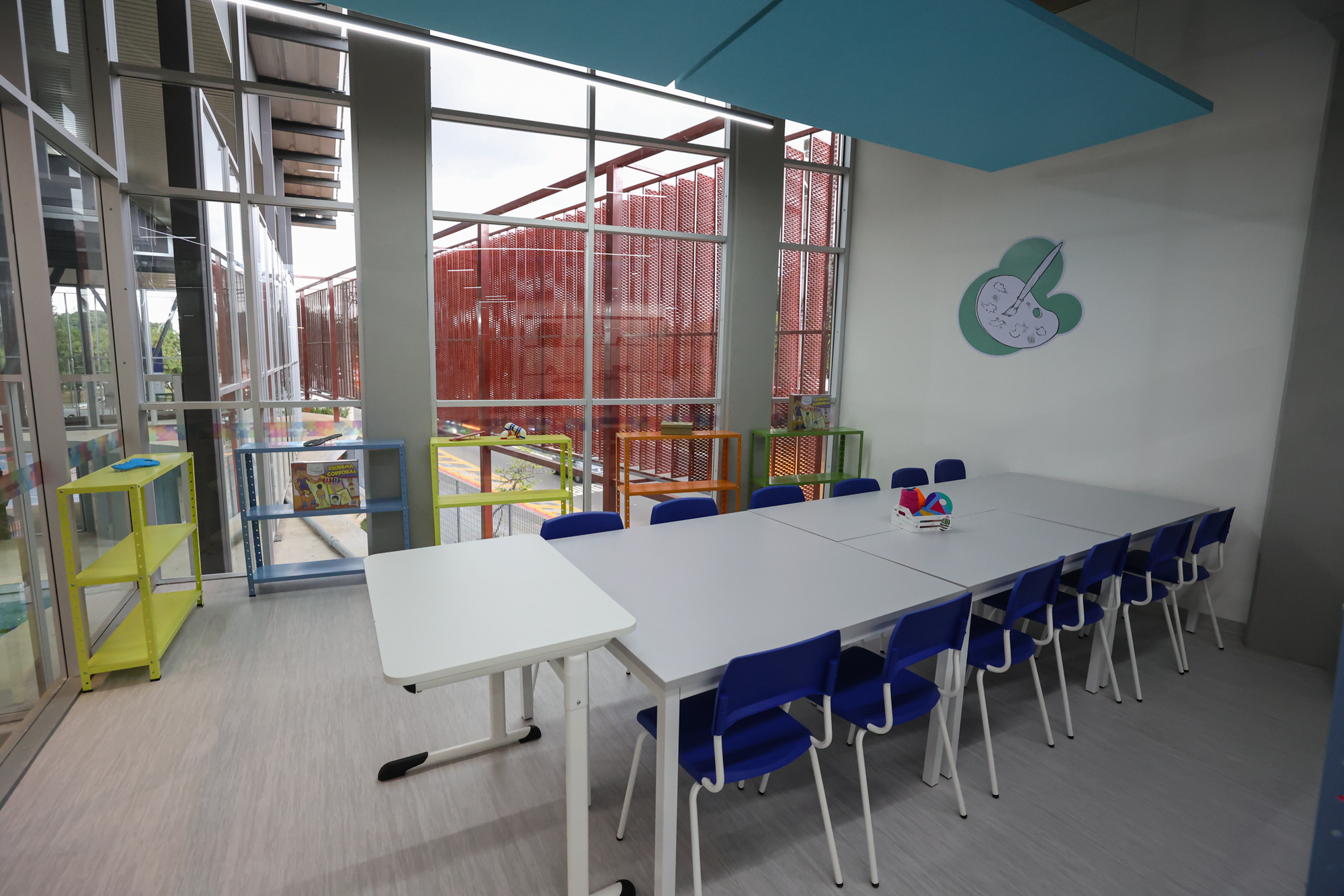 Imagem da sala de oficinas do Centro TEA. Nela há mesas, cadeiras, armários, estantes com objetos e tapete.