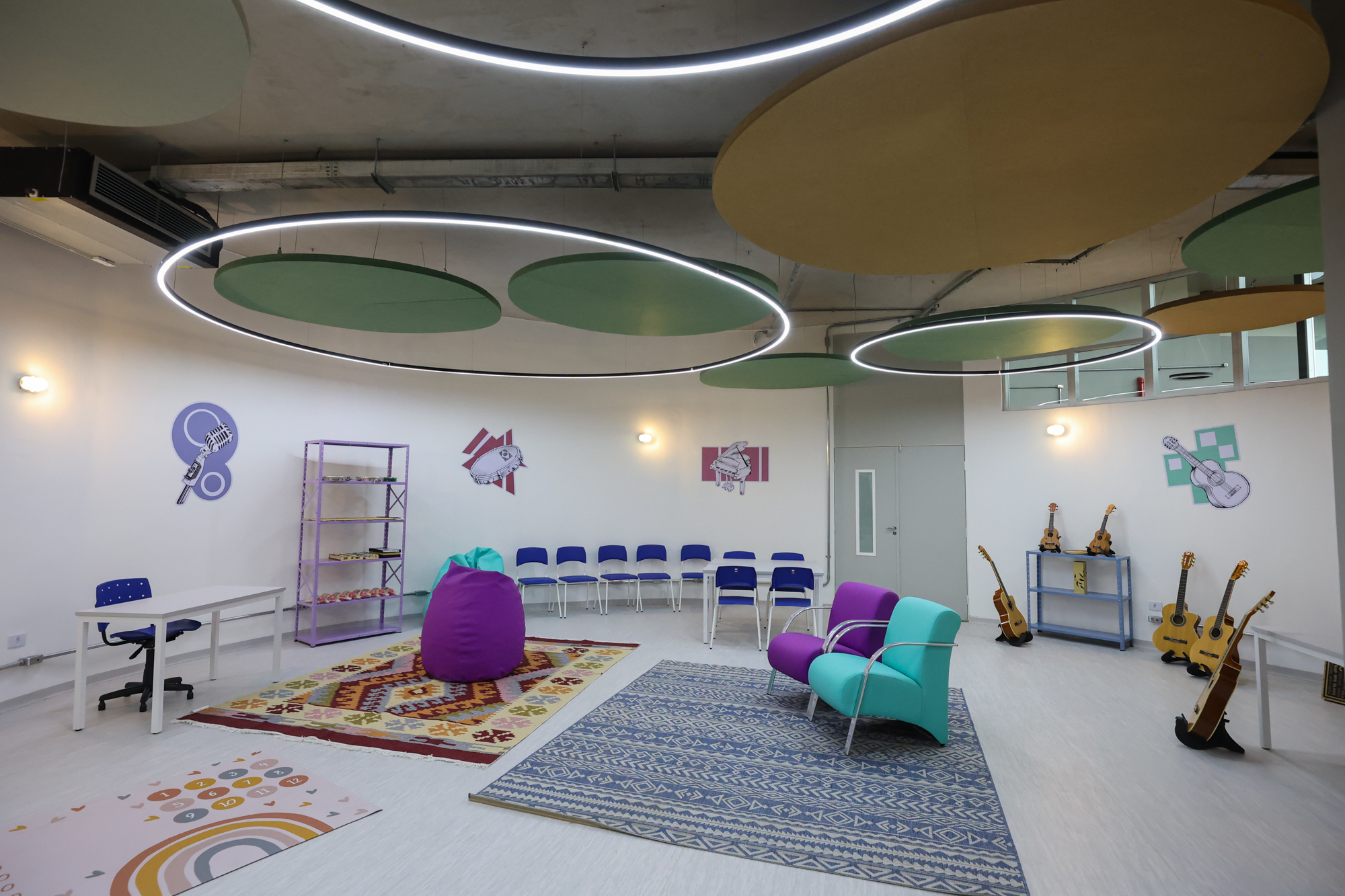 Imagem da sala de música do Centro TEA. Nela há diversos instrumentos como violão, cavaquinho, maracas. Além de tapete, mesas e cadeiras.