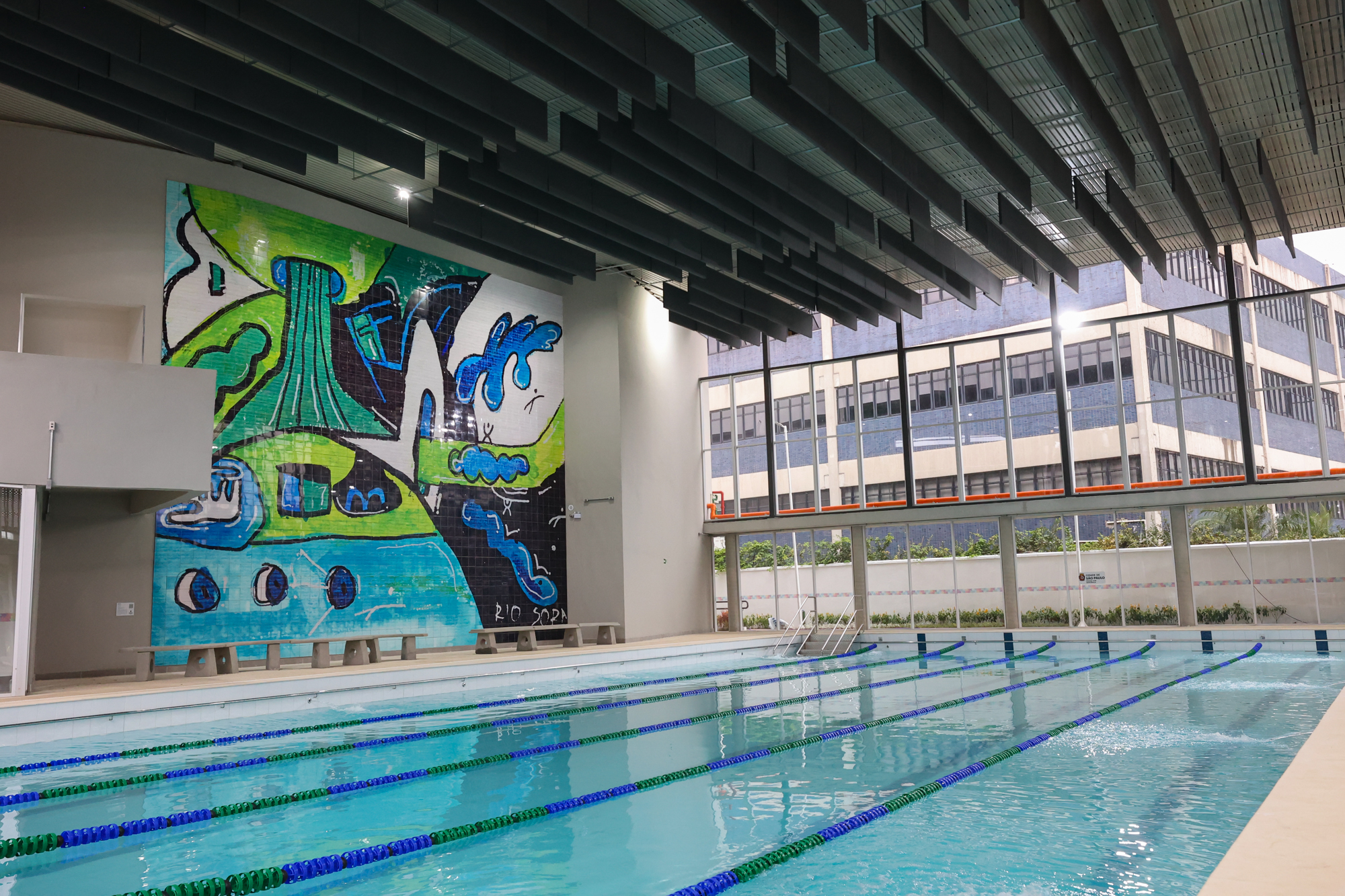 Imagem da piscina do Centro TEA. A piscina está com as raias. Em volta há bancos e azulejos que formam uma obra artística.