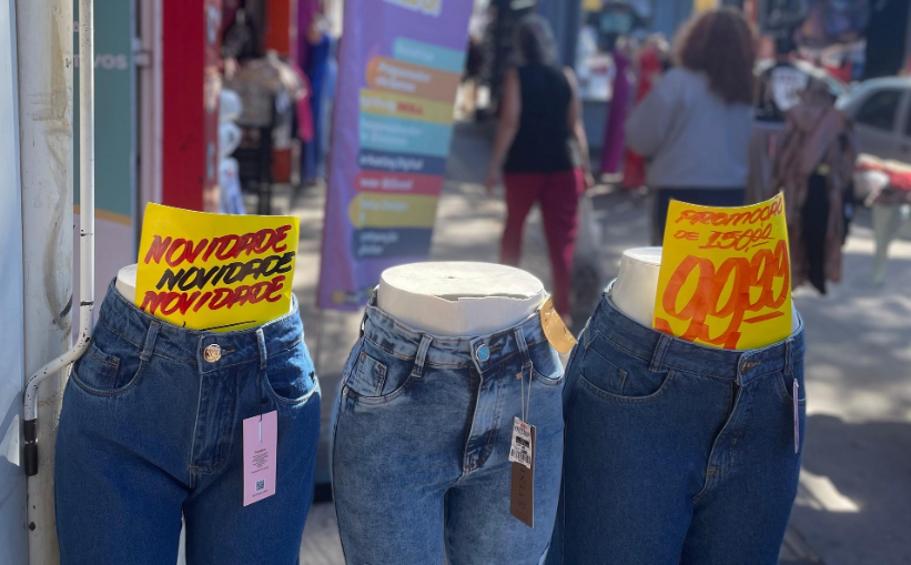 Três manequins vestindo calças jeans nas cores azul escuro, azul médio e azul escuro respectivamente. No primeiro, uma placa em amarelo escrito 