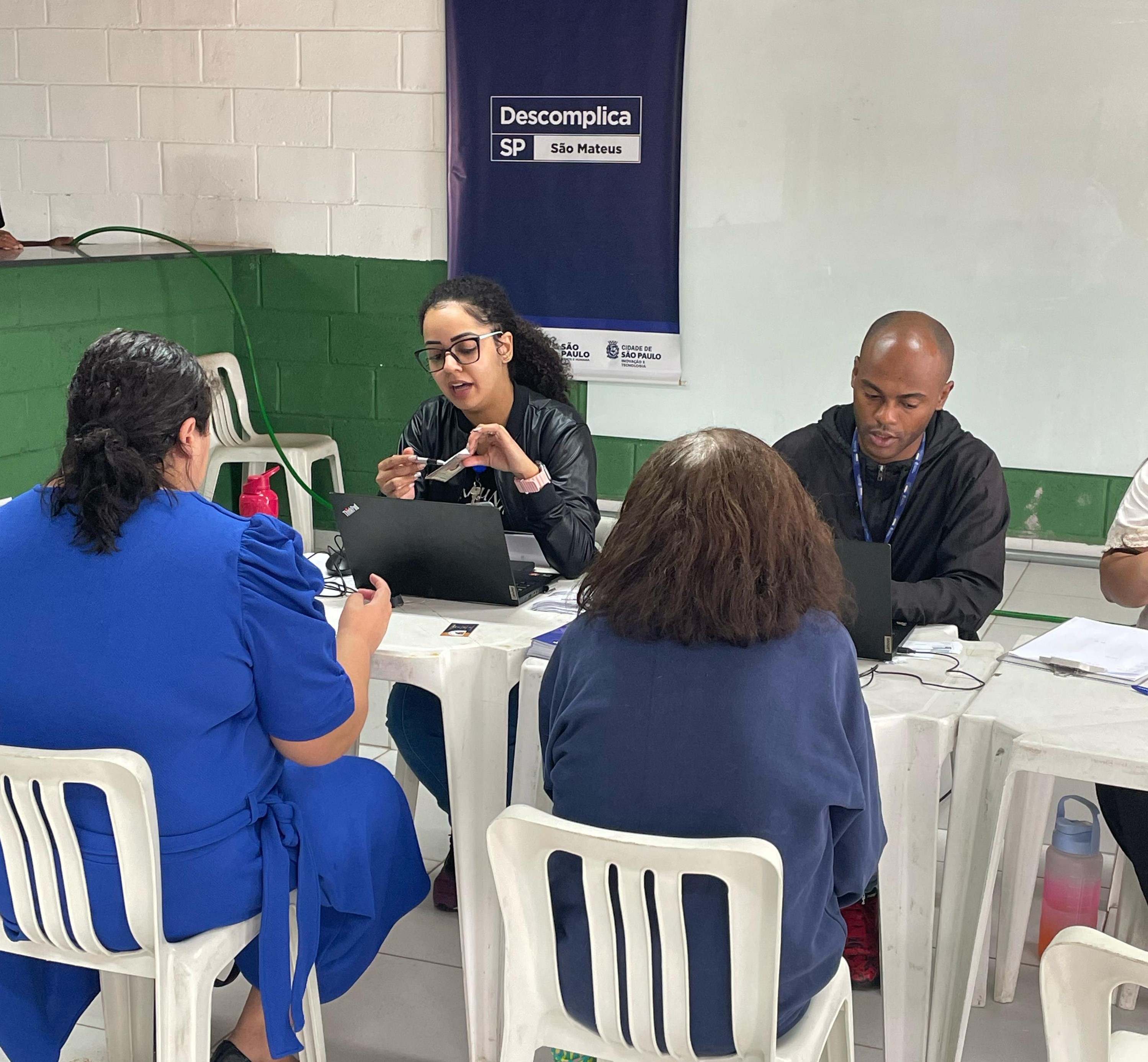 dois trabalhadores do descomplica entre mesas anotando os dados de municipes, que estão na frente