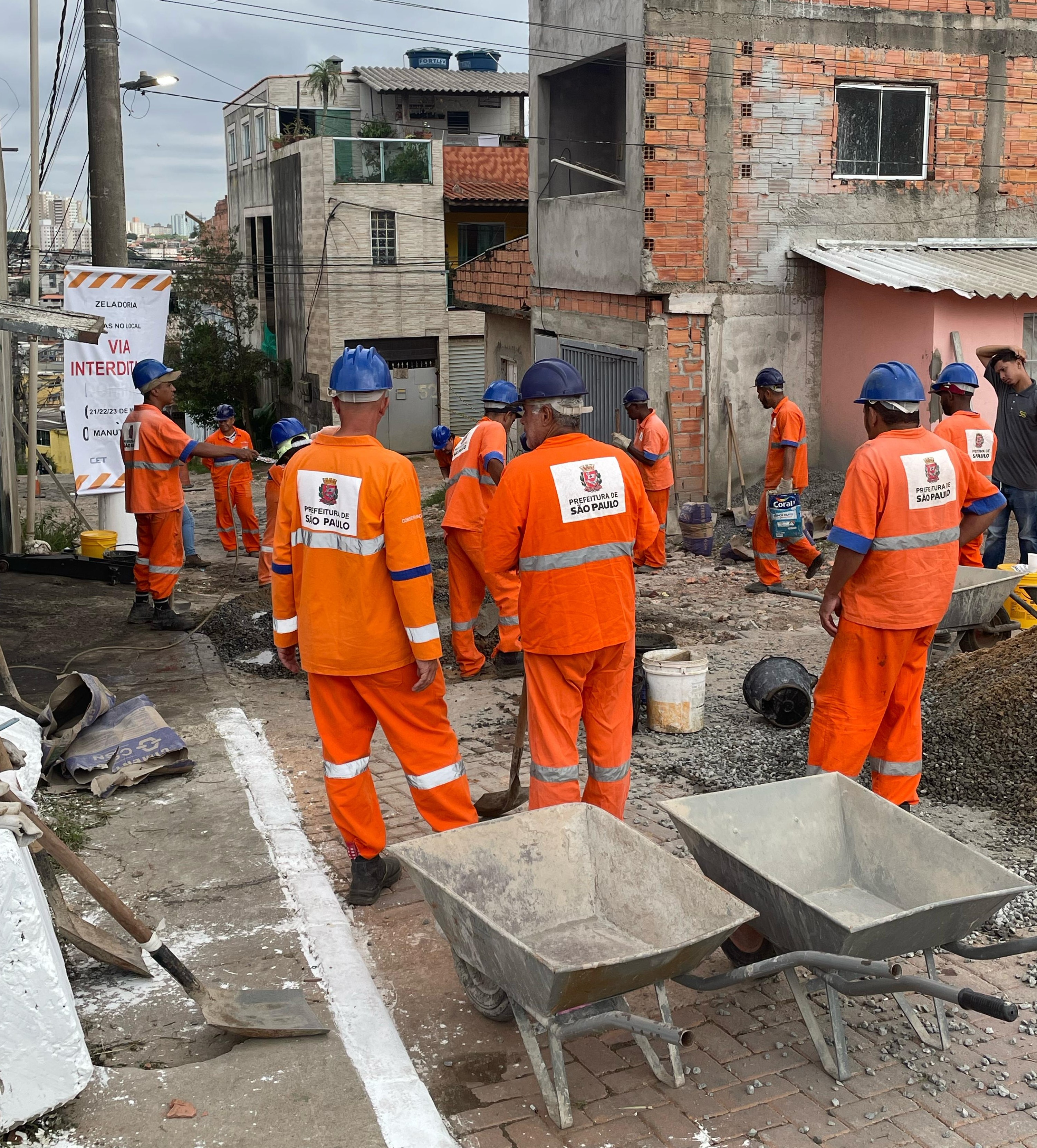por volta de 10 homens trabalhando na obra de uniforme laranja