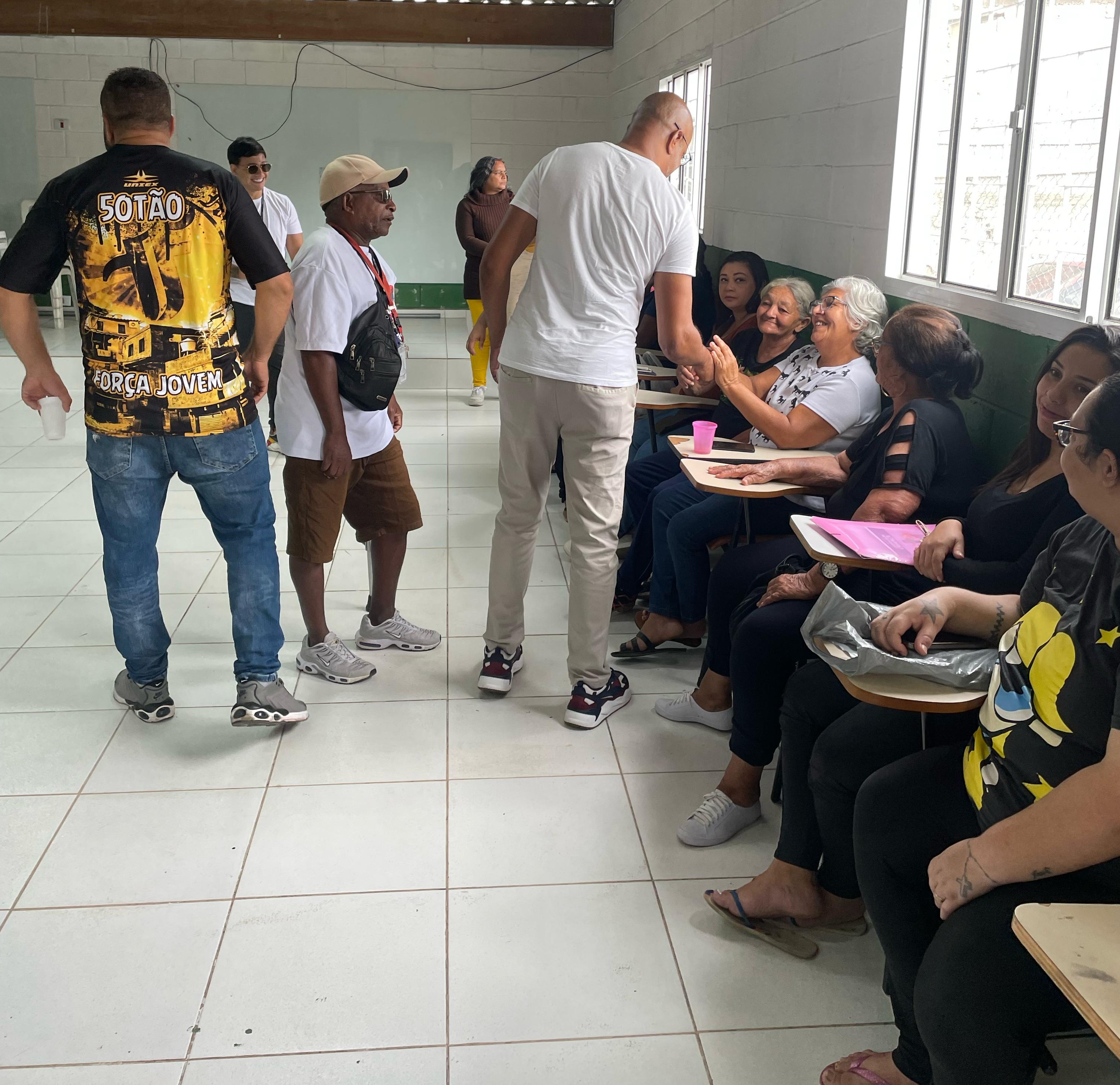 O Subprefeito Ozziel de costas cumprimentando municipes dentro de uma salao iluminado com janelas e luzes naturais
