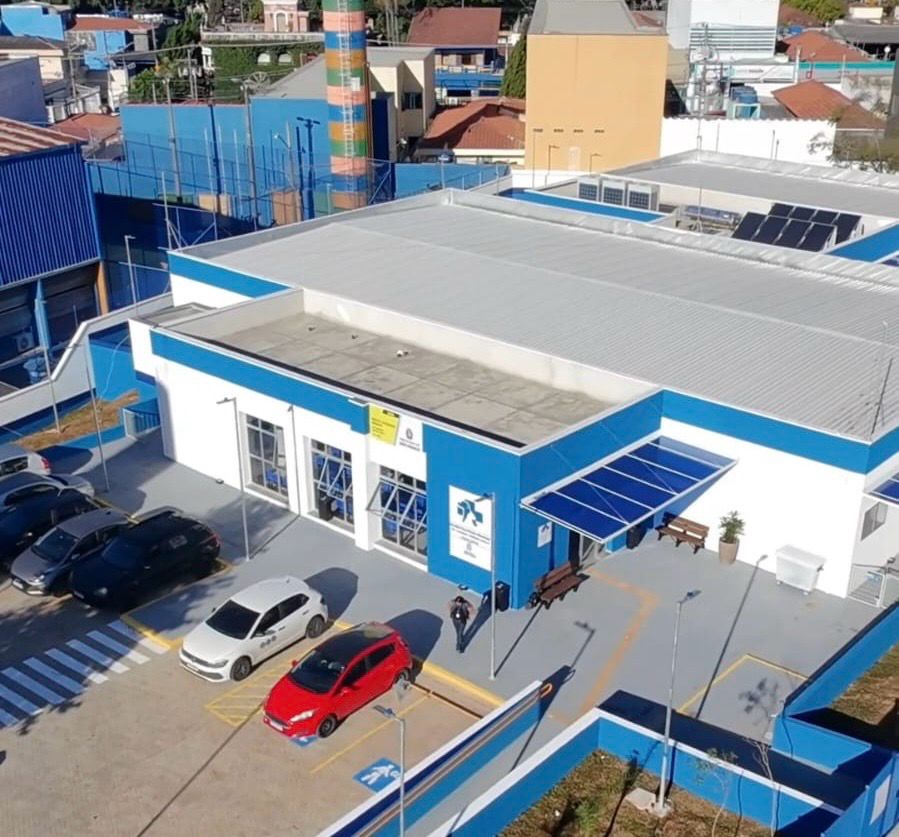 Hospital Veterinário Público “Cão Caramelo”, unidade de atendimento veterinário com fachada azul e branca. A imagem mostra a área externa do prédio, com estacionamento, calçadas de acesso e cobertura na entrada principal, destacando a estrutura destinada ao atendimento de animais.