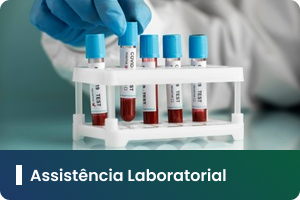 Pra Todos Verem: Card com fotografia de ambiente laboratorial. Em primeiro plano, uma mão utilizando luva azul segura um tubo de coleta. Ao centro, há um suporte branco contendo vários tubos de ensaio com amostras de sangue identificadas por etiquetas. O fundo aparece desfocado, destacando os materiais utilizados em exames e análises clínicas. Na faixa inferior em degradê azul e verde, está o texto: “Assistência Laboratorial”.