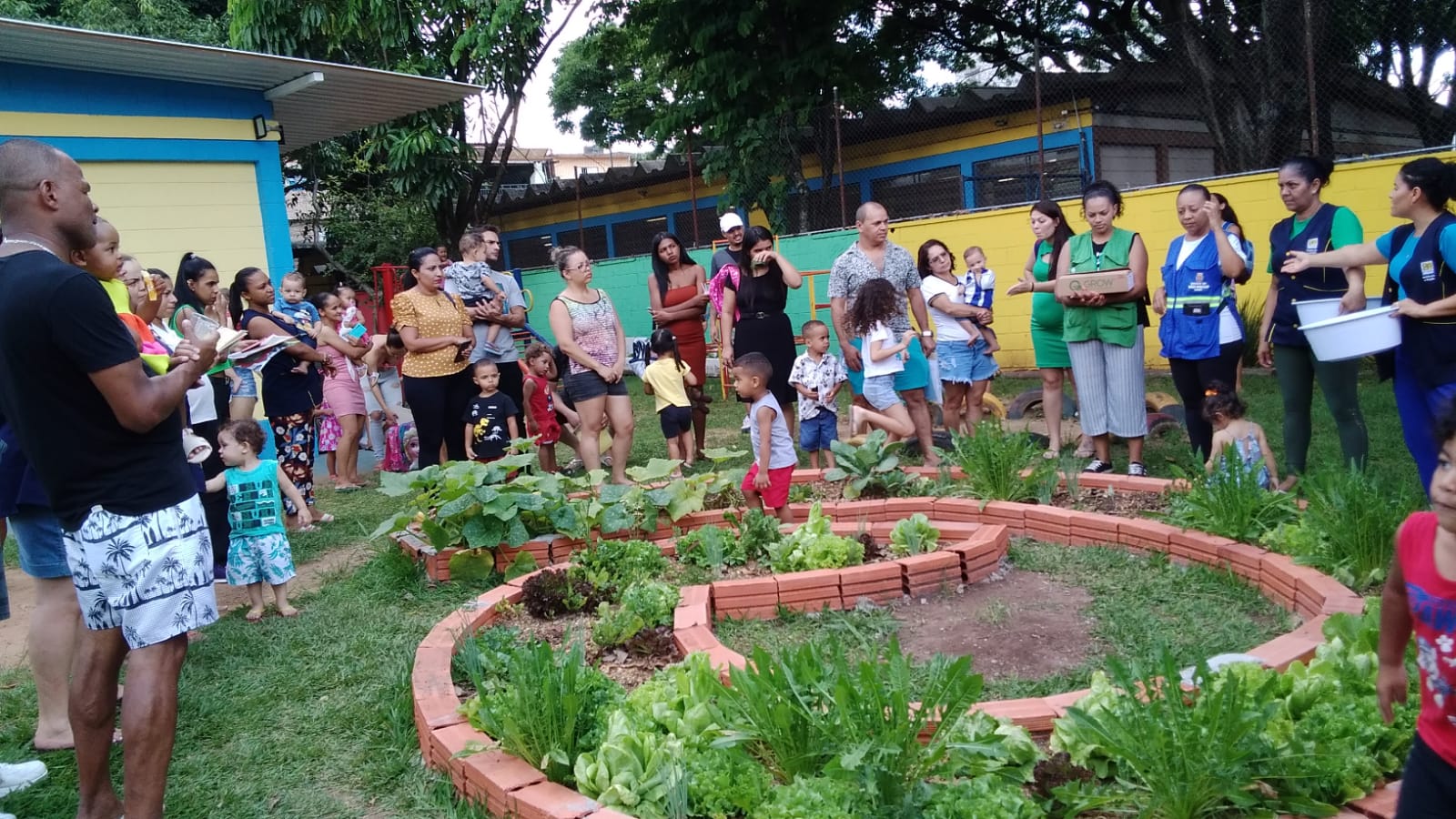 Imagem mostra adultos e crianças praticando jardinagem supervisionadas por profissional.