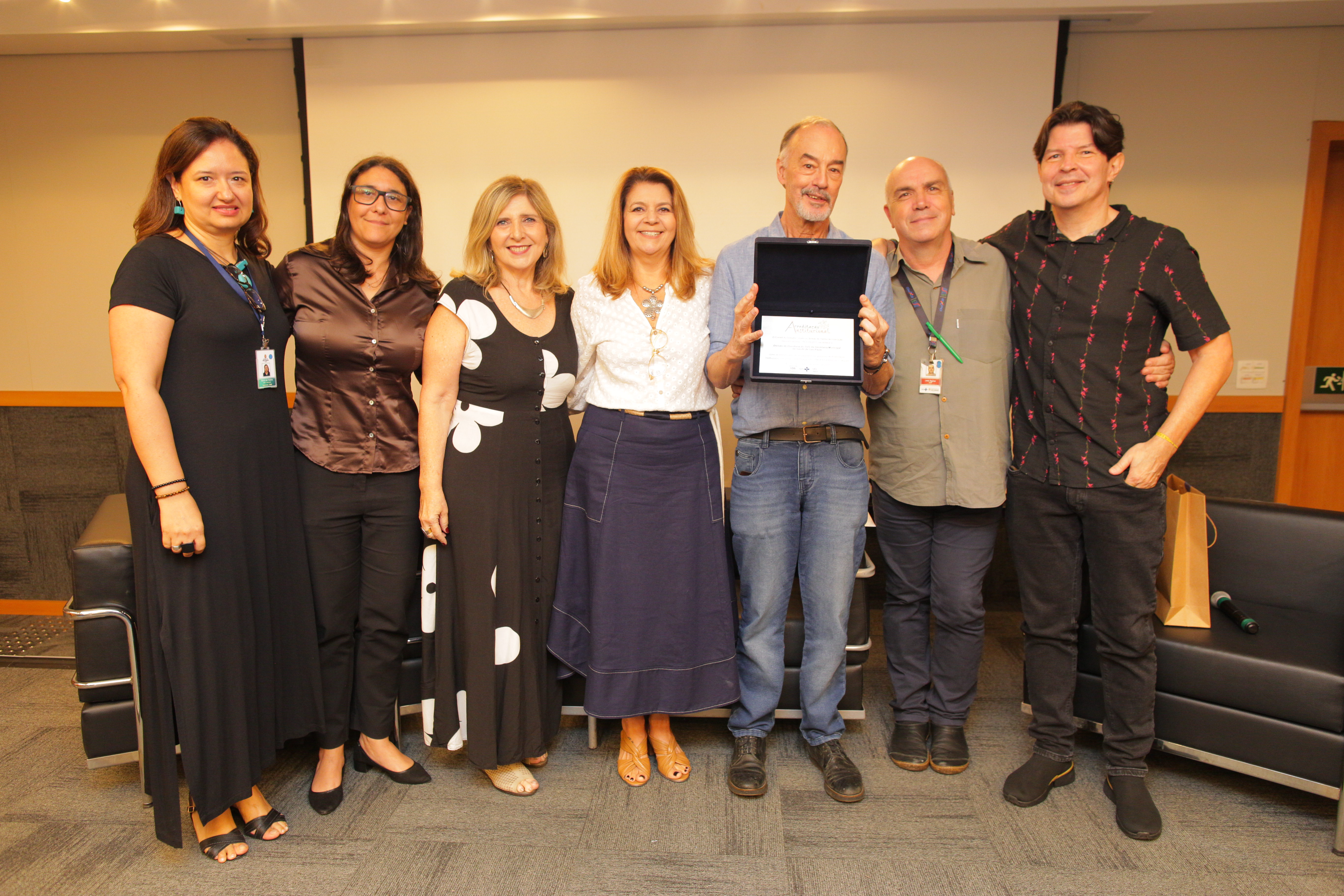 A imagem mostra a equipe da Rede de Ouvidoria segurando uma placa de reconhecimento à creditação.