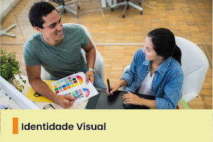 A imagem mostra duas pessoas conversando, uma delas segura uma cartela de cores e a outra uma mesa para desenhos digitais. 