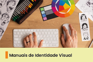 A imagem mostra uma pessoa manuseando um computador, com um material colorido na mesa. 