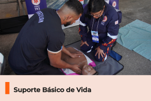 A imagem mostra uma pessoa recebendo treinamento de uma profissional sobre primeiros socorros em um boneco. Abaixo, uma faixa com o texto 
