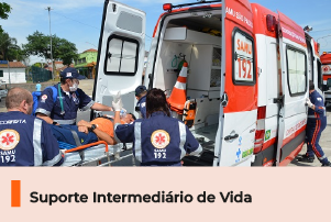 A imagem mostra profissionais da saúde posicionando um paciente em maca dentro de uma ambulância. Abaixo, uma faixa com o texto 