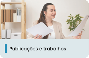 A imagem mostra uma mulher jovem em um escritório segurando papeis, vestindo uma camiseta branca e casaco bege. 