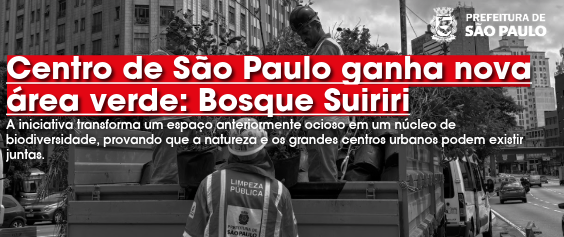A imagem horizontal em tons de cinza mostra trabalhadores da Prefeitura de São Paulo em uma via urbana movimentada. No primeiro plano, de costas, um trabalhador usa colete refletivo com a inscrição 