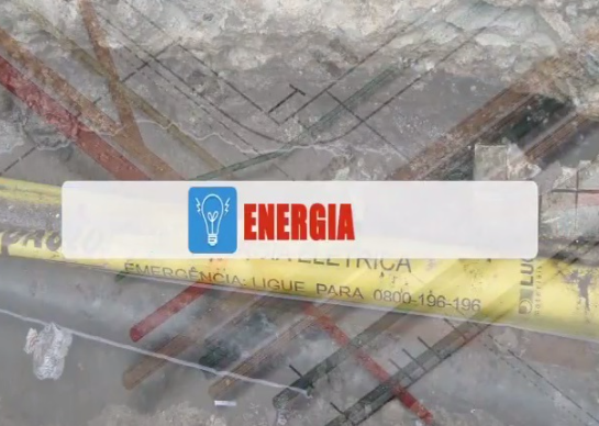A imagem é uma montagem visual com sobreposições. No centro, uma faixa retangular branca com bordas azuis é o foco principal. À esquerda dessa faixa, há um ícone azul de uma lâmpada acesa. À direita do ícone, a palavra "ENERGIA" está escrita em letras maiúsculas e vermelhas. O fundo da imagem é uma mistura desfocada e transparente de vários elementos. É possível distinguir o que parecem ser cabos elétricos ou tubulações em tons de amarelo, vermelho e preto, alguns com inscrições parcialmente visíveis como "EMERGENCIA LIGUE PARA 0800 196-196". Há também linhas que sugerem um projeto ou diagrama técnico, além de texturas que remetem a superfícies de concreto ou solo com detritos, dando a impressão de um canteiro de obras ou infraestrutura.
